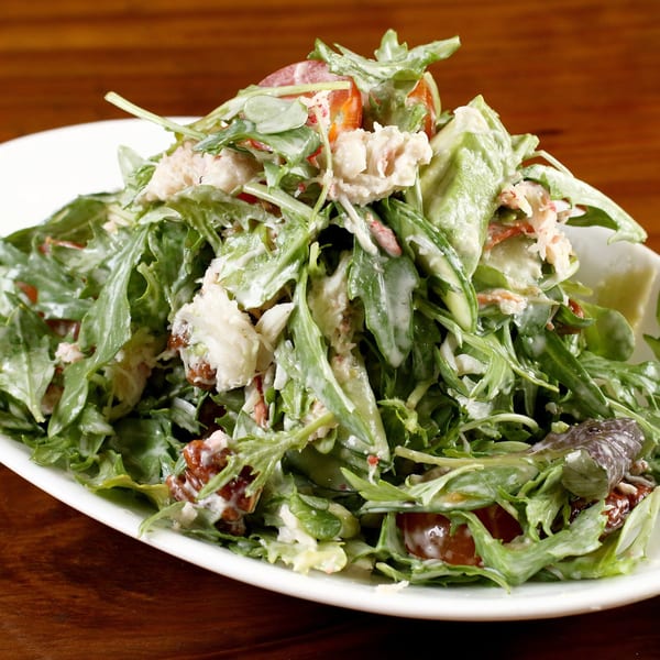 A fresh crab salad with mixed greens, tomatoes, and creamy dressing on a white plate.
