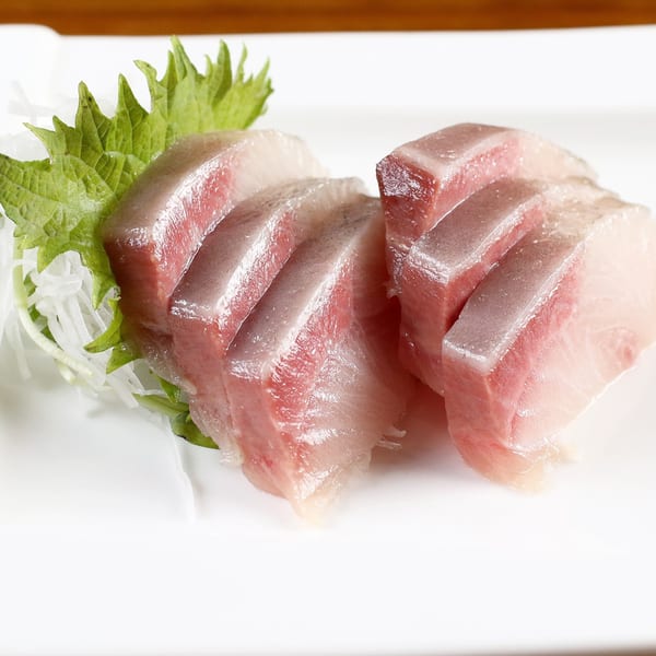 Close-up of fresh, thinly sliced sashimi, garnished with green shiso leaf and white daikon radish.