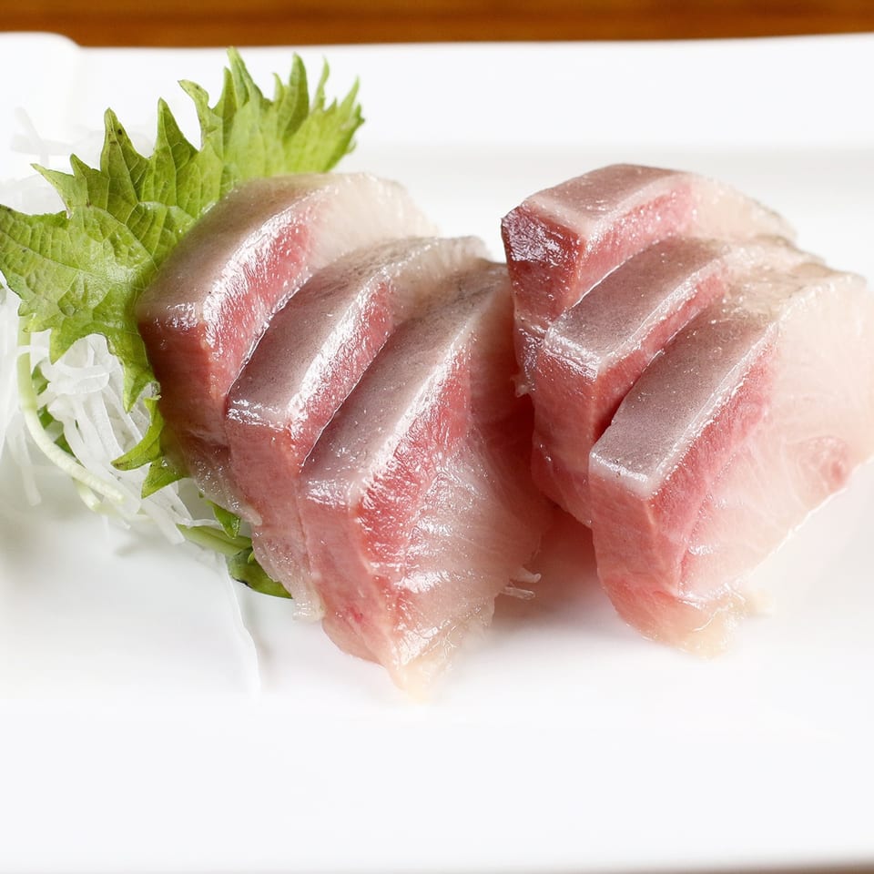 Close-up of fresh, thinly sliced sashimi, garnished with green shiso leaf and white daikon radish.