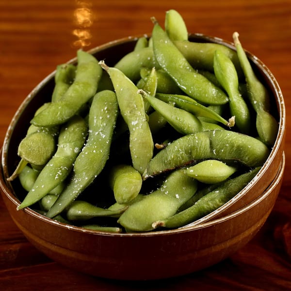 A brown bowl filled with bright green, salted edamame pods on a dark wooden surface.